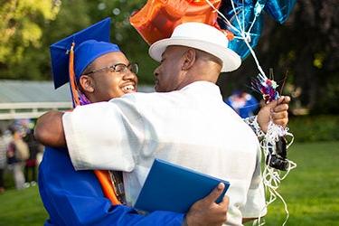 在毕业典礼上，一名学生戴着学士帽和学士服拥抱了一位大人 