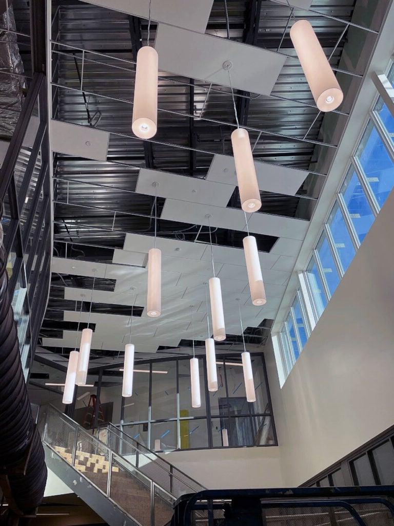 tubular ceiling lights hang from a high ceiling with a stairway below them