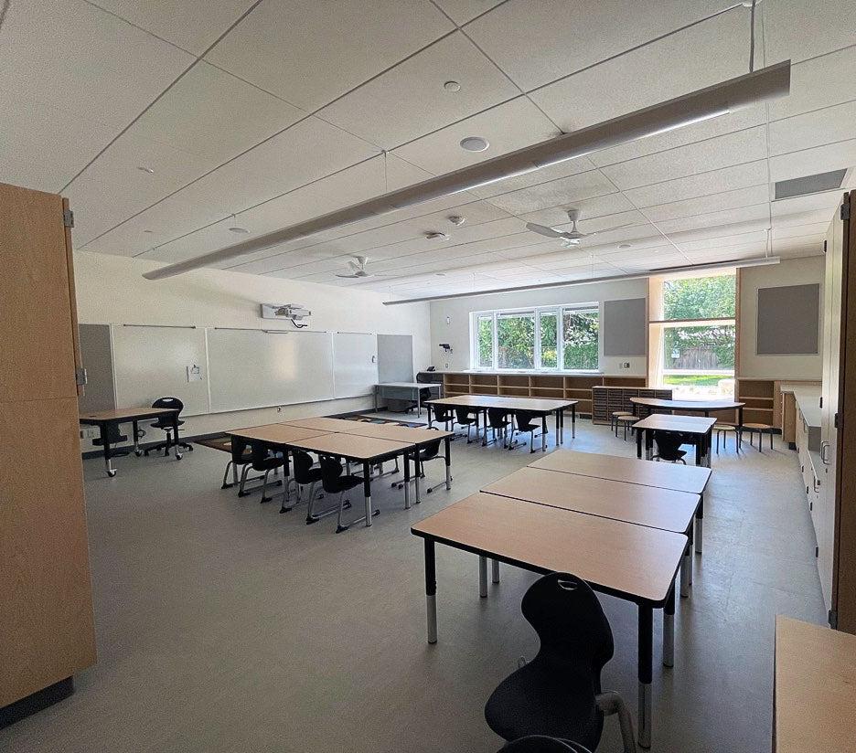 a classroom has groups of tables with chairs, bookcases, whiteboards, lighting and ceiling fans